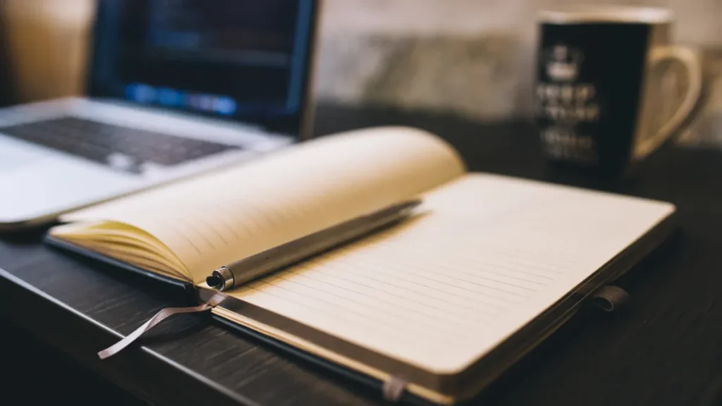 open notebook and pen beside a laptop