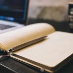 open notebook and pen beside a laptop