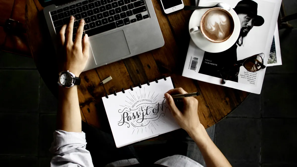 person writing in a notebook at a desk with laptop