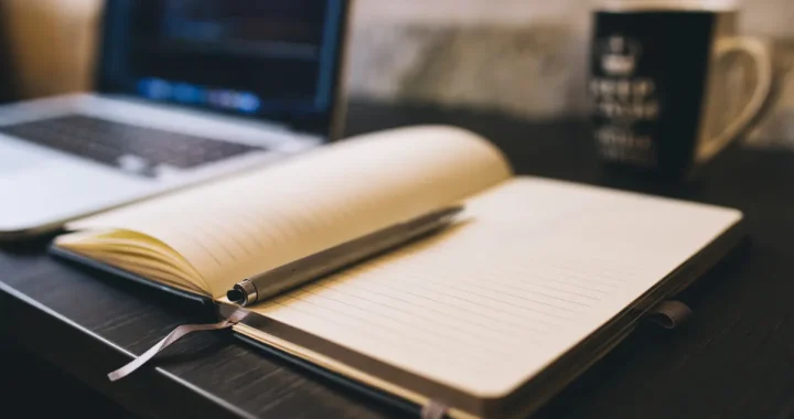open notebook and pen beside a laptop