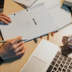 Hands holding a booklet labeled BRIEF beside a laptop